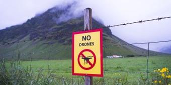 A sign reading "No Drones" is attached to a fence in a grassy field