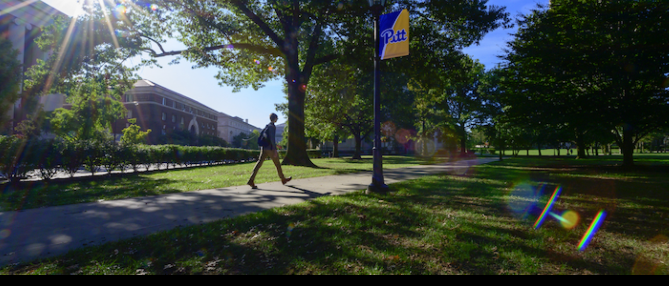 student walking across campus near Pitt flag